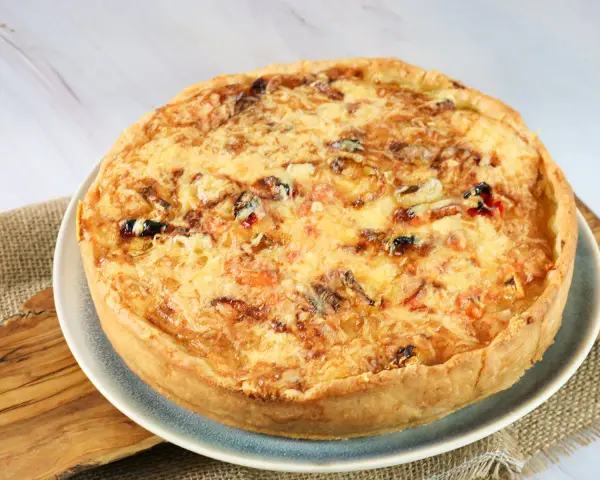 Eine goldbraune Sommer Quiche mit geschmolzenem Käse und bunten Gemüsestückchen, bereit zum Genießen.