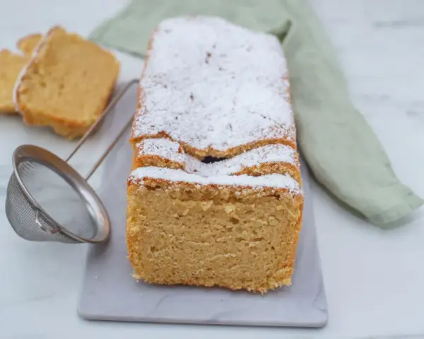 Puszyste keto ciasto z mikrofali, posypane cukrem pudrem, prezentuje się apetycznie. Obok leżą dwa kawałki ciasta i sitko.