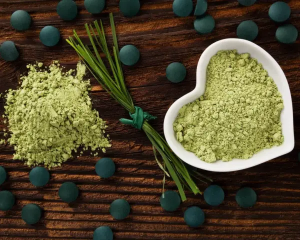 Zielony proszek i tabletki na drewnianym tle. Dowiedz się, spirulina co to za superfood!