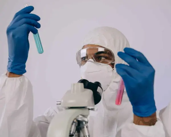 Badacz w kombinezonie i masce analizuje próbki w probówkach, przygotowując się do pracy w laboratorium chemicznym.