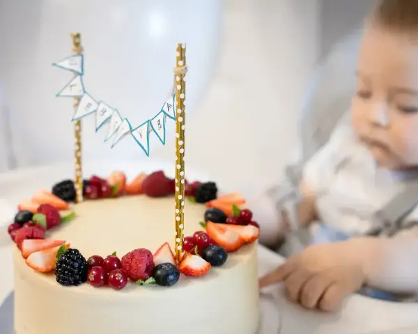 Słodki tort z owocami na przyjęcie dla dzieci. Maluch z zaciekawieniem patrzy na pyszny deser.