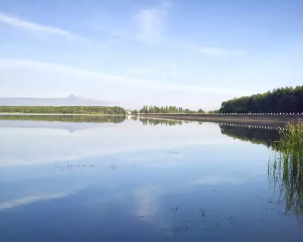 Spokojny zalew Dziećkowice z odbijającymi się w tafli wody chmurami i zielonym lasem w tle.