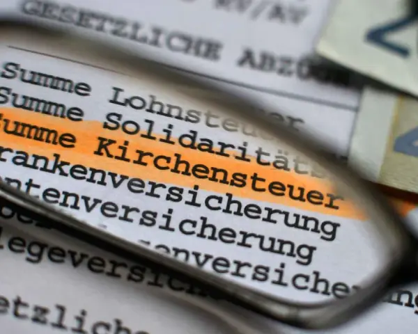 Lupe über Dokument mit hervorgehobener Kirchensteuer. Geld liegt daneben.