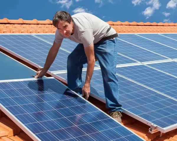 Instalator montuje panele fotowoltaiczne na dachu. Pokazuje, jak zamontować panele fotowoltaiczne, by czerpać energię ze słońca.