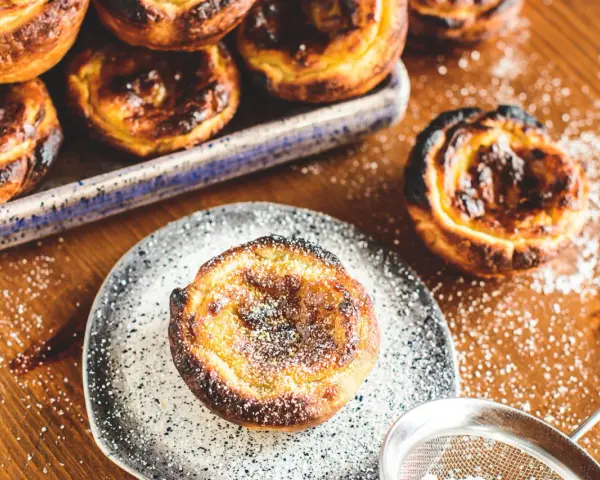 Leckeres Pastel de Nata Rezept: goldbraune Törtchen mit Puderzucker bestäubt, bereit zum Genießen.