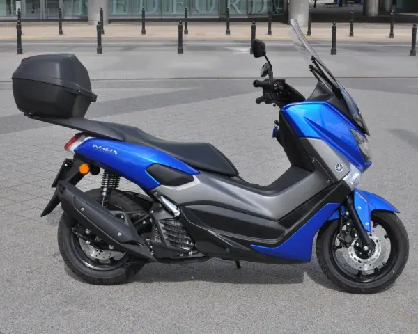 Niebieski skuter Yamaha NMAX 125 z kufrem, gotowy do jazdy. Jego prędkość maksymalna pozwoli na szybkie przemieszczanie się po mieście.