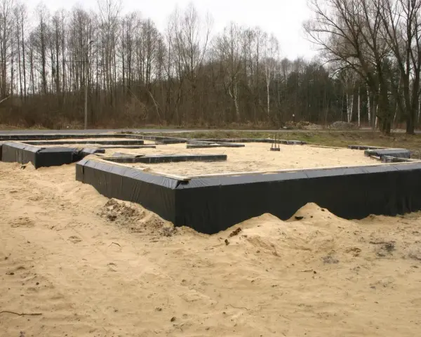 Gotowe ławy fundamentowe otoczone czarną folią, czekają na zalanie betonem. W tle las.