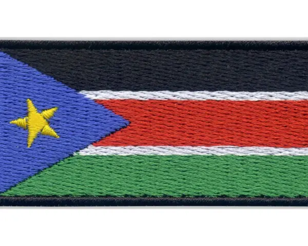 Naszywka z flagą Sudanu Południowego. Czarny pas na górze, pod nim biały, czerwony i zielony pas. Z lewej strony niebieski trójkąt z żółtą gwiazdą.