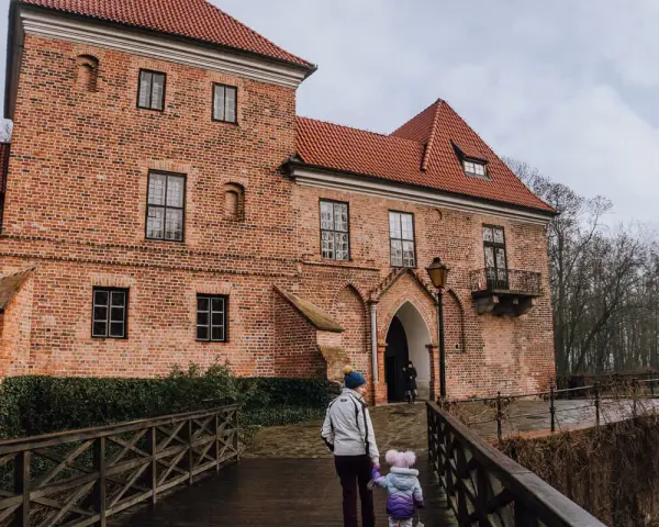Rodzina idzie drewnianym mostkiem do ceglanego zamku w Oporowie.