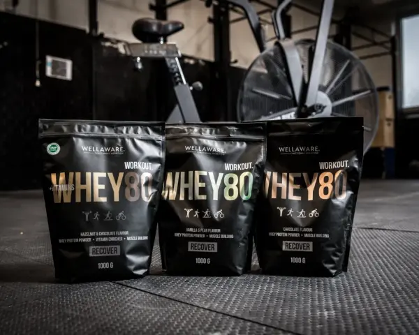 Tre påsar med Wellaware Whey80 proteinpulver står uppradade på ett gymgolv. Perfekt för återhämtning efter träning, oavsett om du föredrar vassle eller kasein.