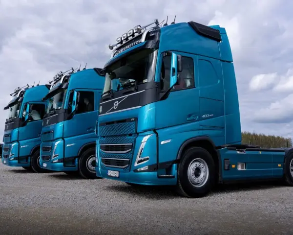 Rząd lśniących, turkusowych ciężarówek Volvo FH gotowych do transportu żywności.