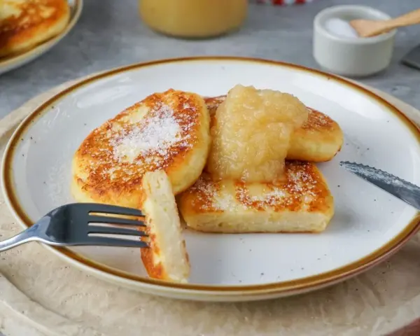 Goldbraune Quarkkeulchen, bestreut mit Zucker, serviert mit Apfelmus. Ein leckeres Quarkkeulchen Rezept zum Genießen.