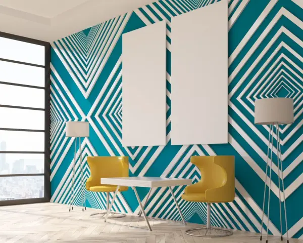Modern room with striking **diseños pared geometrica** in teal and white. Two yellow chairs and a table sit before the wall, with floor lamps and blank canvases.