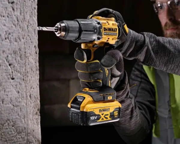 Mężczyzna w rękawicach wierci w betonie najmocniejszą wkrętarką DeWalt 18V XR.