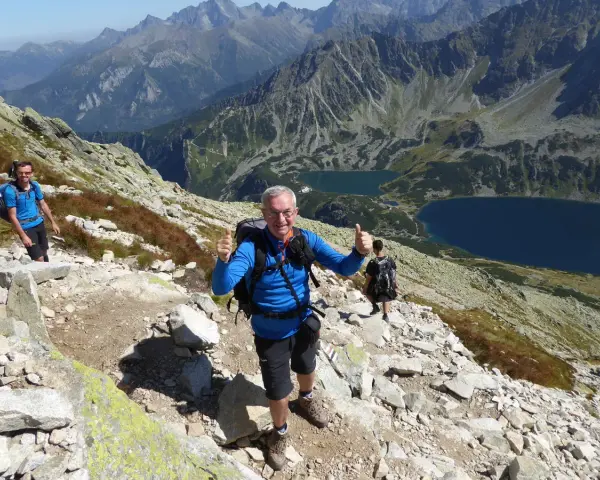 Trasa na Kozi Wierch. Dwóch turystów z plecakami na skalistym szlaku, w tle piękne tatrzańskie jeziora.