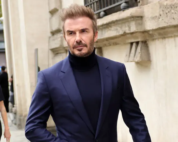 David Beckham luce un elegante traje azul con jersey de cuello alto, caminando con confianza.