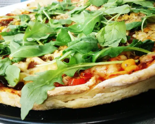 Pyszna pizza z rukolą, pomidorami i serem, pachnąca ziołami. Idealna na szybki obiad.