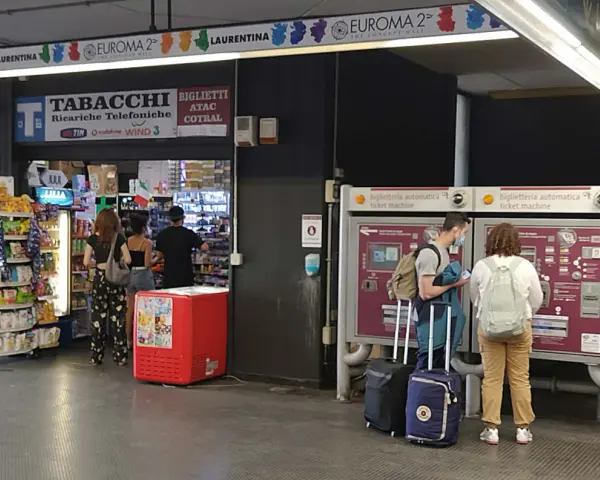 Na dworcu w Rzymie Ciampino ludzie kupują bilety i artykuły w sklepie.