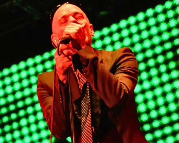 Wokalista REM, Michael Stipe, śpiewa na scenie, gdy światła migoczą na zielono.