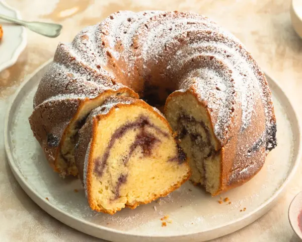 Ein Gugelhupf mit Marmelade, bestäubt mit Puderzucker. Ein Stück ist bereits angeschnitten und zeigt die köstliche Füllung.