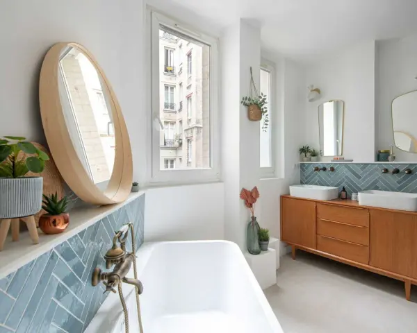 Salle de bain moderne avec carrelage zellige bleu canard, baignoire, double vasque sur meuble vintage et miroir rond en bois. Inspiration zellige.