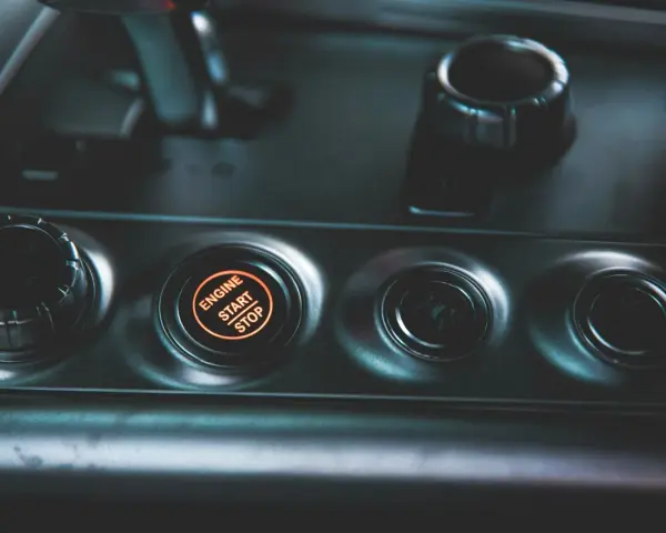 Podświetlany przycisk "ENGINE START STOP" w samochodzie. Obok niego pokrętło wyboru trybu jazdy, jak czujnik IBS.