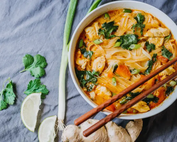 Miseczka z tajską zupą curry z kurczakiem, makaronem ryżowym i warzywami, podana z pałeczkami.