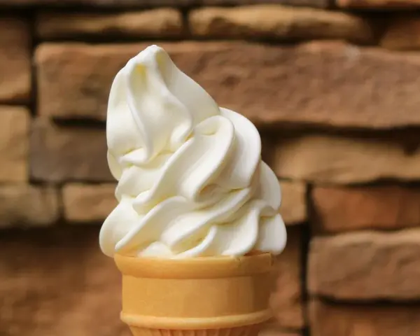 Ein cremiges Vanilleeis mit Ei im Waffelhörnchen, vor einer rustikalen Steinwand.