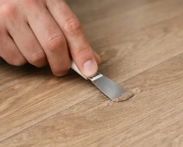 Mano che ripara un piccolo buco nel muro con una spatola e stucco.