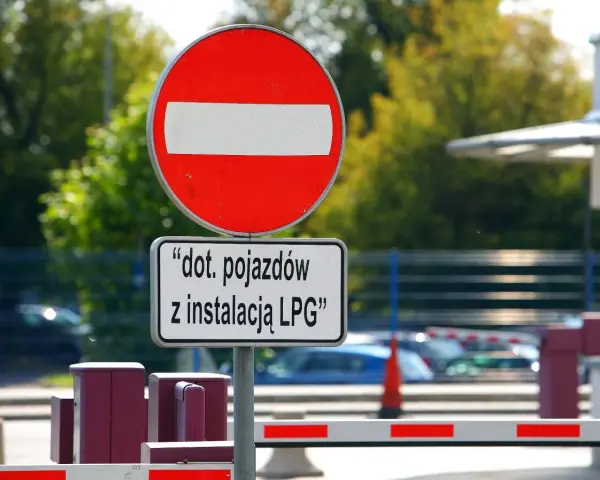 Znak B2 "zakaz wjazdu" z tabliczką informującą, że dotyczy pojazdów z instalacją LPG. Za znakiem widać szlaban i samochody.