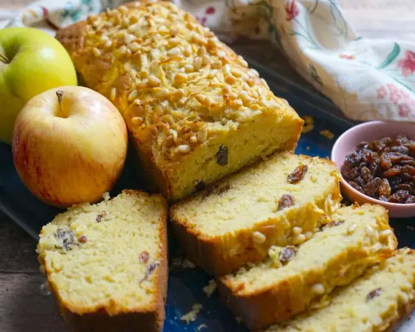 Plumcake alle mele dorato, con pinoli e uvetta, accompagnato da mele fresche e una ciotolina di uvetta.