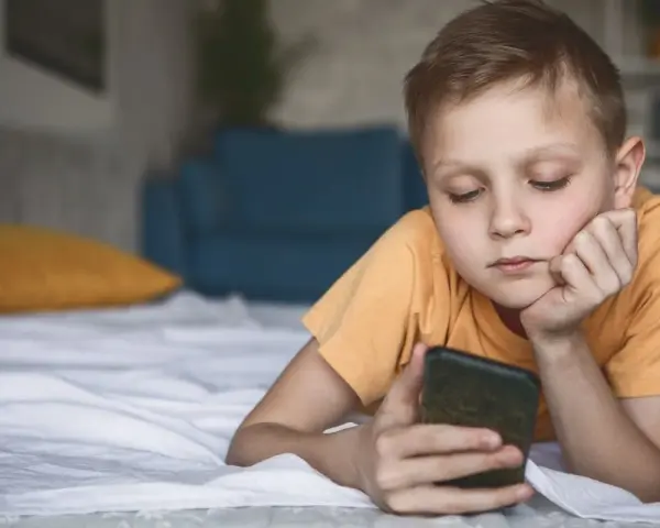 Chłopiec leży na łóżku, patrząc na telefon. Zastanawia się, co to jest sexting i jakie niesie zagrożenia.