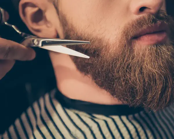 Un barbero recorta una barba larga y rojiza con tijeras.