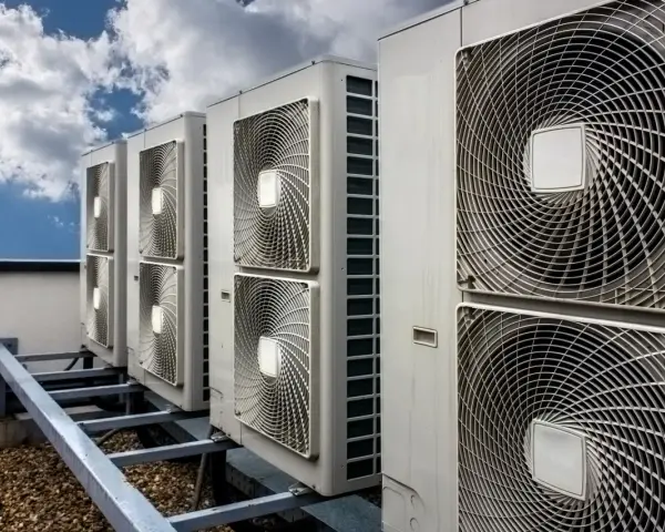 Rząd jednostek klimatyzacyjnych na dachu pod błękitnym niebem z chmurami.