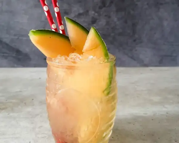 Orzeźwiający drink z mango, ozdobiony plasterkami owocu i dwoma czerwono-białymi słomkami. Idealny na upalne dni.