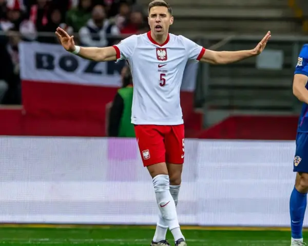 Piłkarz w białej koszulce z orłem, numer 5. Jan Bednarek po kontuzji wraca do gry, gestem prosi o spokój.