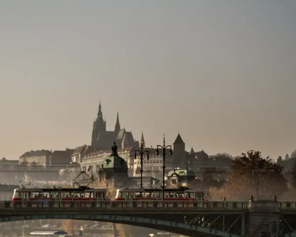 Most w Czechach, po którym przejeżdża tramwaj, z widokiem na zabytkowe budowle w oddali.