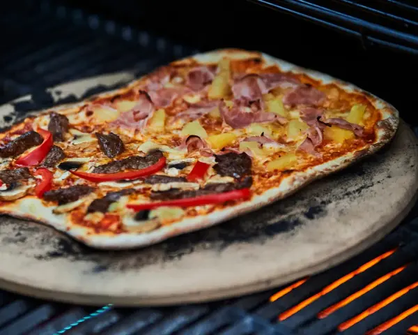En läcker pizza på grillen med skinka, ananas, kött och paprika. En perfekt sommarmåltid!
