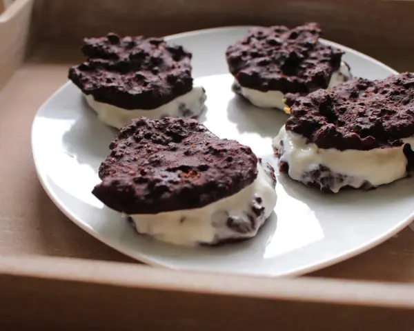 Cztery domowe ciastka z kremem, przypominające Oreo, na białym talerzu. Pyszna przekąska, choć warto sprawdzić oreo kcal przed zjedzeniem.