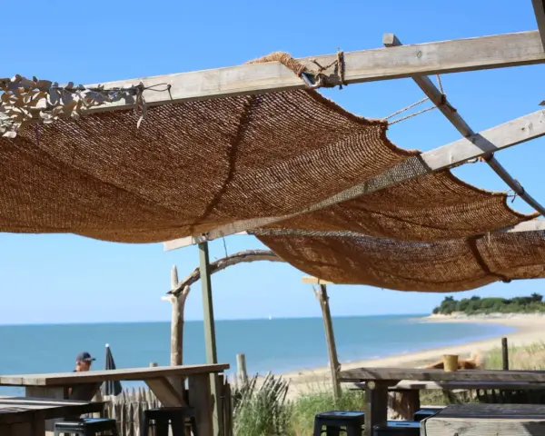 Installation d'une voile d'ombrage en toile de jute sur une structure en bois, offrant une vue sur la mer et la plage.