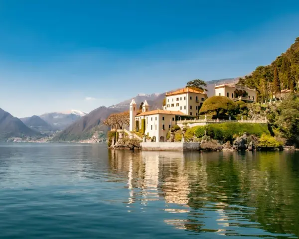 A scenic journey from Milan to Lake Como reveals this stunning villa on the water's edge, with mountains in the distance.