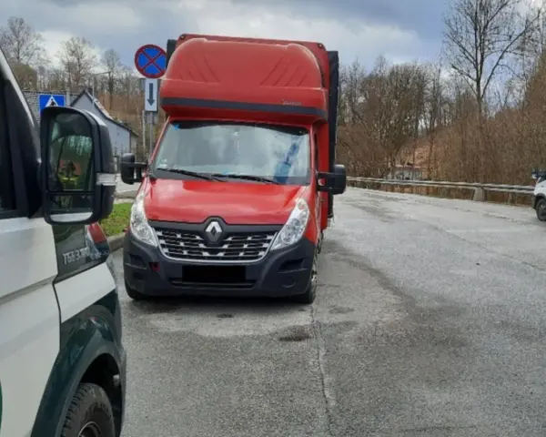 Czerwony bus Renault na drodze, obok pojazd inspekcji. Może to być związane z wnioskiem o wypis z licencji transportowej.