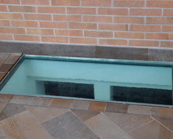Bocche di lupo moderne in vetro, incastonate in un pavimento di piastrelle color terra, illuminano uno spazio sottostante.