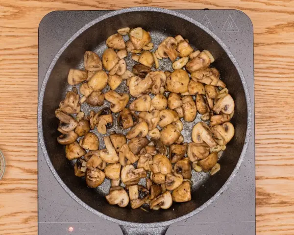 Champiñones al ajillo dorándose en sartén, con ajo y perejil picado al lado.