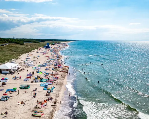 Słoneczna plaża w Darłówku pełna ludzi, kolorowych parawanów i namiotów. Woda w Bałtyku błyszczy, a fale zachęcają do kąpieli. To idealne miejsce na wakacyjne atrakcje.