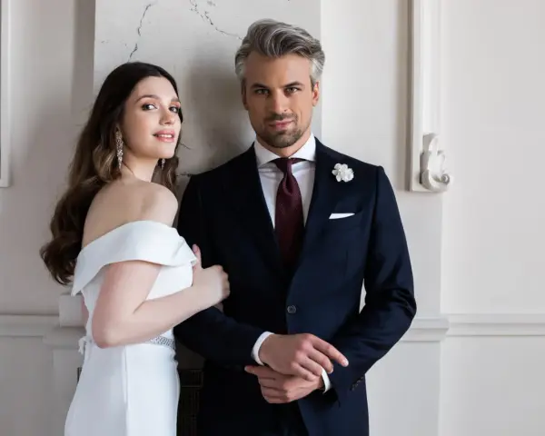 Elegancki pan młody ślub cywilny w granatowym garniturze i jego uśmiechnięta narzeczona w białej sukni.
