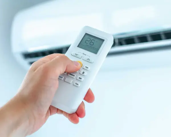 Dłoń trzymająca pilot do klimatyzatora, ustawiająca temperaturę. Ogrzewanie klimatyzatorem to komfort.