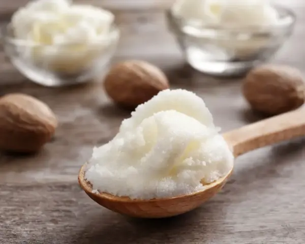 Ein Holzlöffel voller cremiger shea butter haare, daneben Nüsse und Schalen mit der Butter.