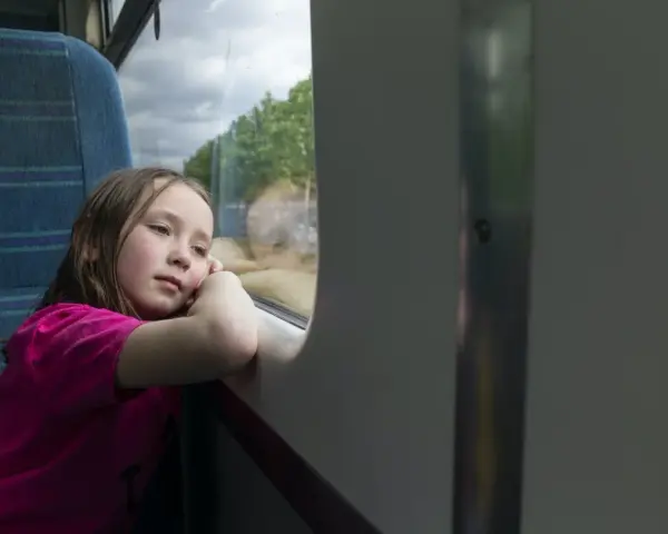 Dziewczynka wpatrzona w okno pociągu, zastanawia się, od ilu lat można jeździć samemu pociągiem.