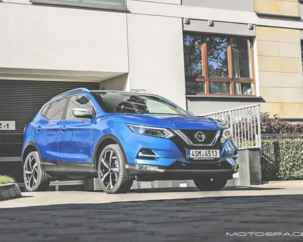 Błękitny Nissan Qashqai 2018 zaparkowany przed nowoczesnym budynkiem z garażem.